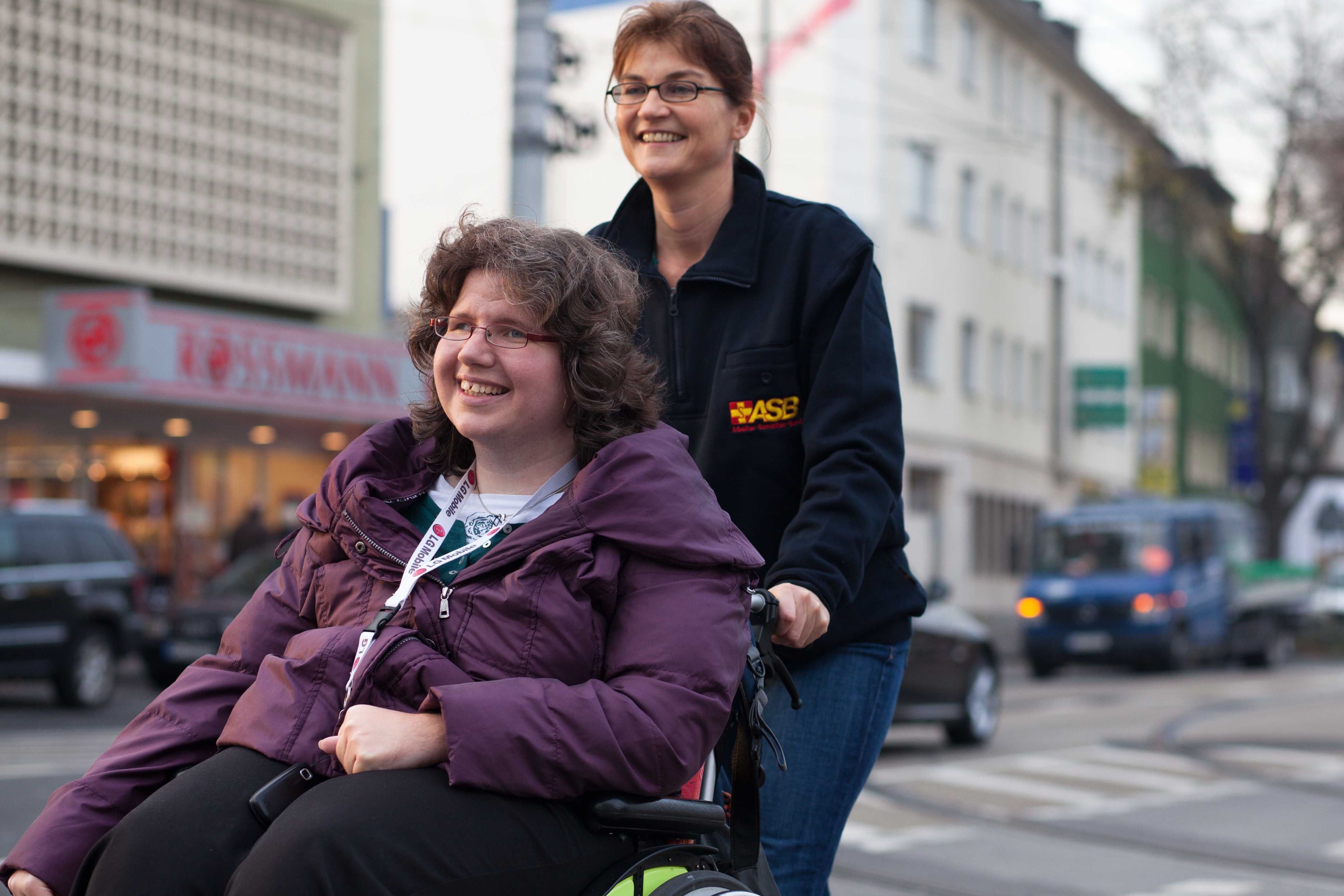 Eine Frau schiebt eine andere Frau im Rollstuhl im Straßenverkehr